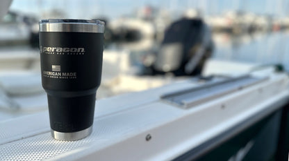Black tumbler with 'Peragon' branding on a boat deck with water and boats in the background